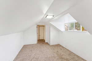Additional living space featuring light carpet and vaulted ceiling