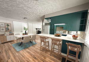 Kitchen featuring light countertops, light wood-type flooring, white appliances, green cabinetry, and a peninsula