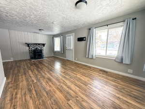 Unfurnished living room featuring a textured ceiling, dark wood finished floors, visible vents, and baseboards