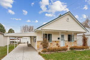 Bungalow-style house with covered porch, a front lawn, concrete driveway, an outdoor structure, and an attached carport