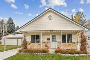 Bungalow featuring a porch, stone siding, and a front lawn