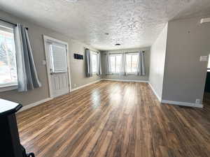 Unfurnished living room with dark wood-style floors, a textured ceiling, and baseboards