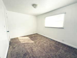 Empty room with visible vents, dark carpet, and baseboards