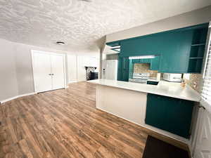 Kitchen with a textured ceiling, a peninsula, white appliances, wood finished floors, and light countertops