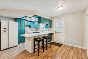 Kitchen featuring white appliances, blue cabinets, a kitchen bar, a textured ceiling, and light wood-style flooring