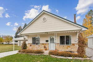 Bungalow-style home featuring a porch, stone siding, and a front lawn