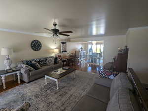 Living room featuring a ceiling fan, crown molding, and wood finished floors