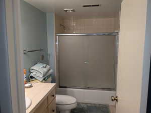 Full bathroom with toilet, bath / shower combo with glass door, visible vents, and vanity