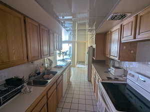 Kitchen featuring tile countertops, light tile patterned floors, white appliances, a sink, and backsplash