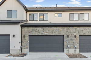 View of back of property with a garage, stone siding, and concrete driveway