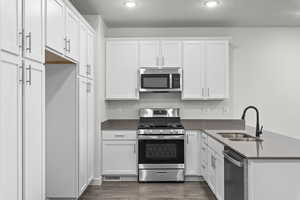 Kitchen featuring dark wood-type flooring, a sink, white cabinetry, appliances with stainless steel finishes, and dark countertops