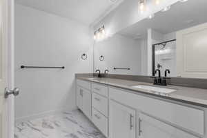 Full bath with marble finish floor, a sink, baseboards, and double vanity