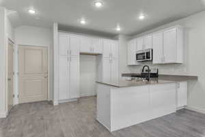 Kitchen featuring appliances with stainless steel finishes, white cabinets, a peninsula, and light wood finished floors