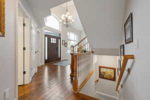 Foyer with dark wood-style floors, lofted ceiling, a chandelier, baseboards, and stairs