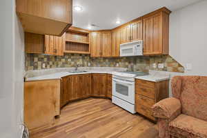 Kitchen with white appliances, a sink, decorative backsplash, light wood finished floors, and brown cabinetry