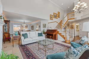 Living area featuring crown molding, a notable chandelier, a towering ceiling, and stairs