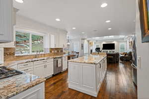 Kitchen featuring stainless steel appliances, a kitchen island, white cabinets, open floor plan, and light stone countertops