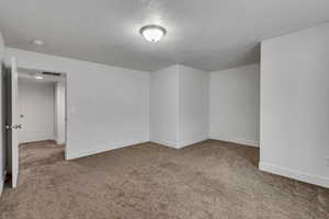 Carpeted spare room featuring a textured ceiling, visible vents, and baseboards