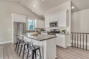 Kitchen with stainless steel appliances, a center island, white cabinets, and light stone countertops