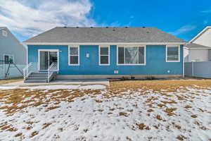 Snow covered back of property featuring roof with shingles, fence, and stucco siding