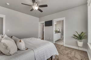 Bedroom with ceiling fan, light colored carpet, visible vents, baseboards, and ensuite bath