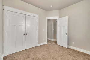 Unfurnished bedroom featuring baseboards, a closet, and light colored carpet