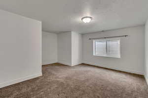 Carpeted spare room with a textured ceiling and baseboards