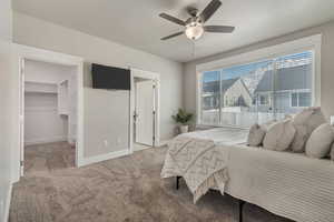 Carpeted bedroom featuring ceiling fan, a spacious closet, ensuite bathroom, and baseboards