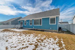 Snow covered house with a yard, a fenced backyard, a gate, and roof with shingles