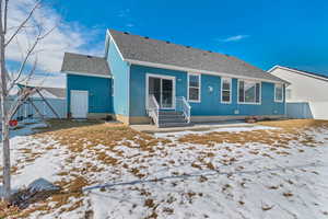 Snow covered rear of property featuring a shingled roof and fence