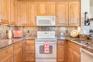 Kitchen featuring white appliances, dark stone countertops, a sink, and tasteful backsplash