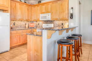 Kitchen with white appliances, light tile patterned flooring, and dark stone countertops