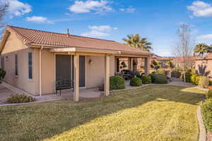 Back of house with stucco siding, a tiled roof, a lawn, and a patio