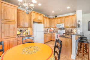 Kitchen with light tile patterned floors, white appliances, visible vents, dark stone countertops, and pendant lighting