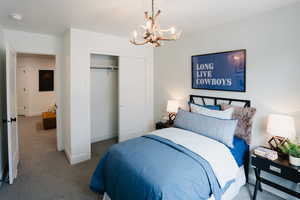 Carpeted bedroom with baseboards, a closet, and a notable chandelier