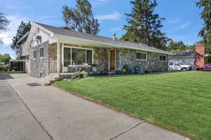 Single story home featuring stone siding, a front yard, cooling unit, and driveway