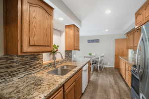 Kitchen with tasteful backsplash, light stone counters, brown cabinets, stainless steel appliances, and a sink