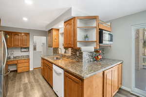 Kitchen with appliances with stainless steel finishes, brown cabinets, a sink, and light stone counters