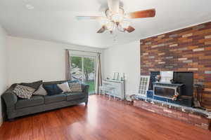 Living room with a ceiling fan, a wood stove, and wood finished floors