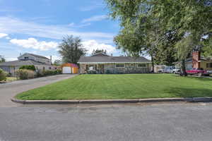 Ranch-style home with an outdoor structure, a detached garage, stone siding, driveway, and a front lawn