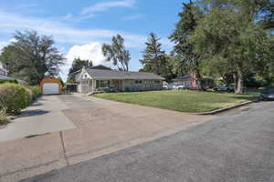 Single story home featuring a front yard, stone siding, driveway, and a detached garage