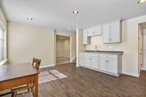 Kitchen with dark wood-style floors, baseboards, a sink, and white cabinets