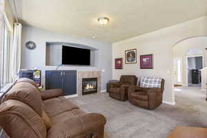 Living area featuring light carpet, baseboards, arched walkways, and a tile fireplace