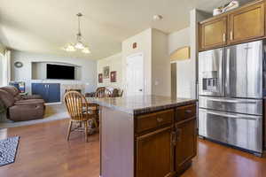 Kitchen with a fireplace, stainless steel fridge with ice dispenser, open floor plan, a center island, and dark countertops