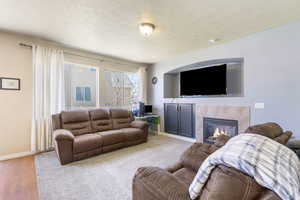 Living room with light wood-style floors, a textured ceiling, baseboards, and a tiled fireplace