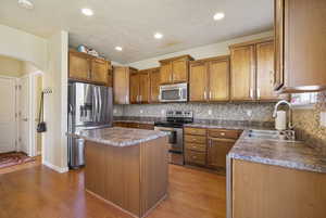 Kitchen featuring arched walkways, a sink, appliances with stainless steel finishes, a center island, and dark countertops