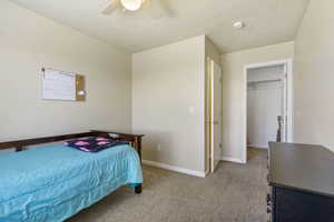 Bedroom with baseboards, ceiling fan, a walk in closet, and light colored carpet