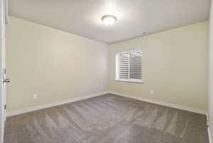 Carpeted spare room featuring a textured ceiling, visible vents, and baseboards