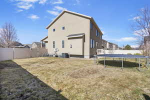 Back of property featuring a trampoline, stucco siding, a lawn, cooling unit, and a fenced backyard