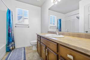 Bathroom with shower / bath combination with curtain, a wealth of natural light, vanity, and toilet